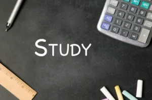 Blackboard with the word Study written in white, surrounded by a pen, ruler, calculator, and colorful chalk.